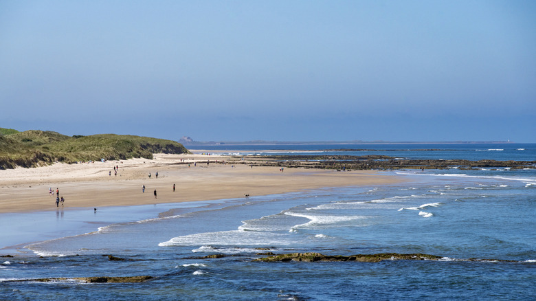 People walking on Seahouses North Beach with Bamburgh Castle in the background in Seahouses, England