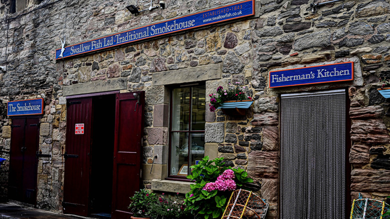 The stone exterior of the historic Swallow Fish Smokehouse adorned with flowers in Seahouses, England