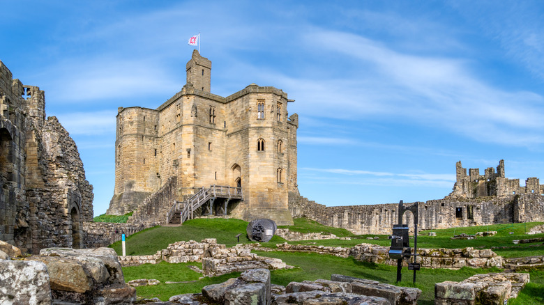 The keep of Warkworth Castle surrounded by ruins under a partly cloudy blue sky in Northumberland
