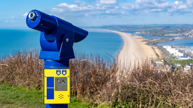 A coin-operated telescope on a hill looking out at the view over Chesil Beach