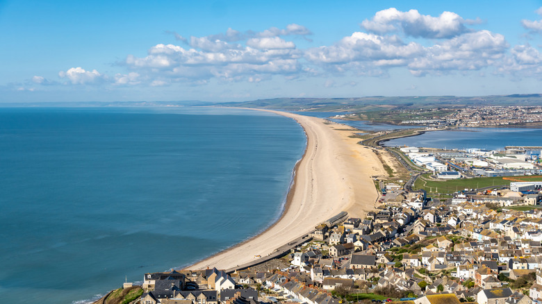 Aerial view of sandy Chesil Beach with buildings along the coast on a sunny day, with some light clouds on the horizon