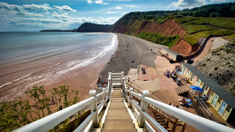 A white wooden staircase leading down to Jacob's Ladder Beach and sunbathers with red cliffs towering over the coast in Sidmouth