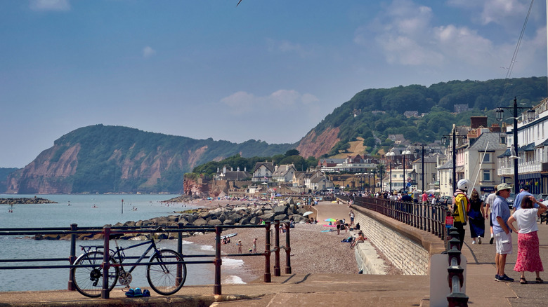 People enjoying Sidmouth's long esplanade, beaches, and calm water, with Regency-era buildings and ancient red cliffs nearby