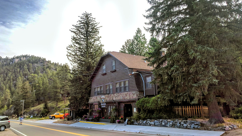 An old-school Colorado inn flanked by large evergreen trees with forested mountains in the background