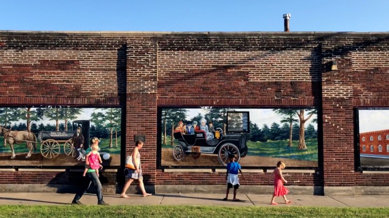 People walk in front of a brick mural sporting Ligonier, Indiana's famous murals
