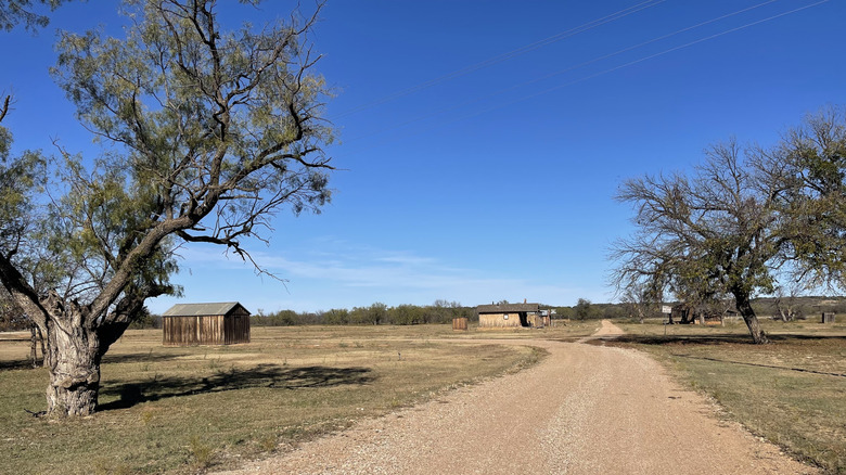 Buildings lie alongside a dirt road leading beneath a blue sky at Fort Griffin