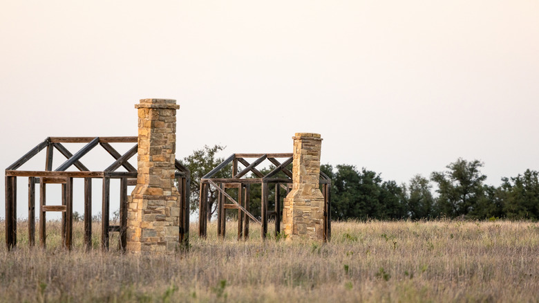Two frameworks of homes in the ruins of Fort Griffin, settled upon grassy plains.