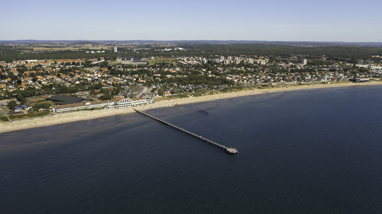 Skea Strand beach in Falkenberg, with a long sand beach, a thin pier reaching into the blue sea, and the low town buildings spreading out behind