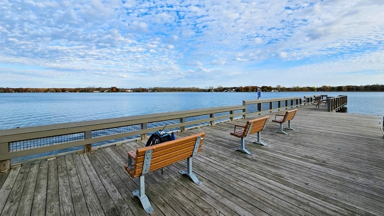 Views of a dock lined with benches, overlooking Lake Lansing in Haslett, Michigan, under a cloudy sky.