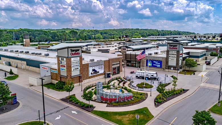 An aerial shot of the outdoor Tanger Outlet Mall, with many shops and a tree-filled hill in the background