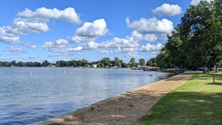 The stretch of sand at Gun Lake Park with the buoyed swim area, vibrant trees, and Gun Lake shoreline in the foreground