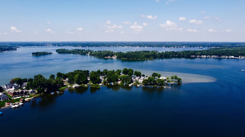An aerial photo of Gun Lake with thin tree-lined peninsulas reaching out into the water and houses lining the shore in the distance