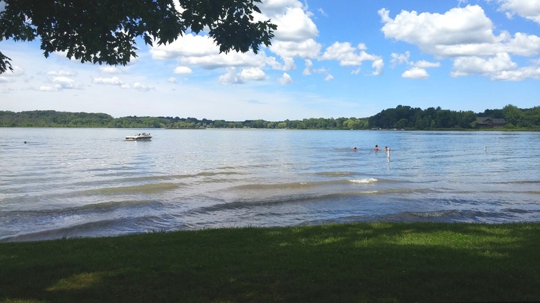 Dumont Lake with green grass in the foreground, a boat on the water, and a few swimmers in the water.