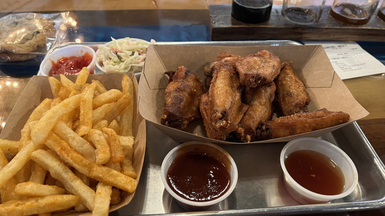 Chicken wings and fries with dipping sauce on a table next to a beer tasting flight at Coopersville Brewing Company