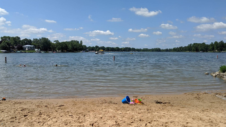 Blue and orange sand pails sit on a sandy beach at Grose Park with Crockery Lake spanning the distance beyond.