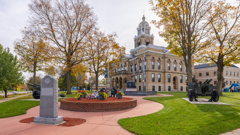 The historic courthouse in Ithaca with a well-kept lawn, tall trees, and a walking path around flower beds, canons, and small monuments