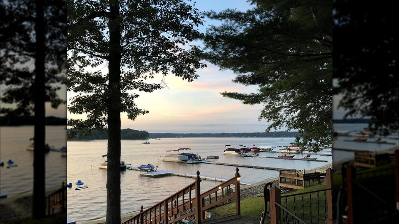 The evening view from a lakeside porch showing a few docks going out into the lake, with trees and the opposite shore in the distance