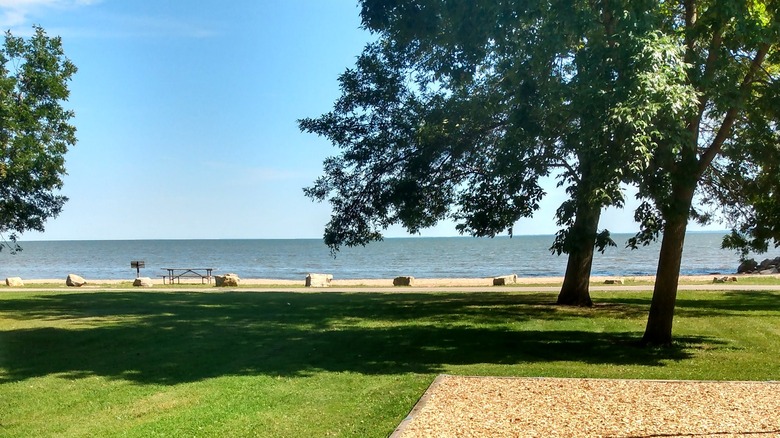 Oconto City Park on Lake Michigan on a sunny summer day, with green grass, a few large trees, and thin sandy beach before the blue water.