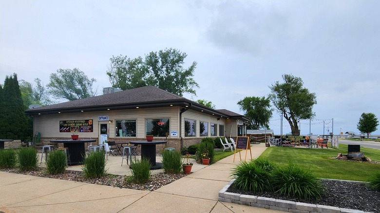 The tan one-story building of the Dockside Restaurant in Ocanto with its clean landscaping, outdoor seating, and the lake off in the distance.
