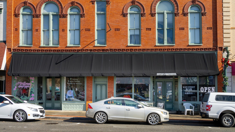 A row of shops below a black awning and red brickwork in downtown South Boston, Virginia, with cars parked on the street.