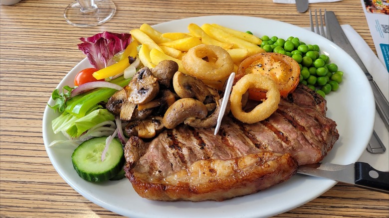 Steak served with onion rings, fries, peas, mushrooms, and a side salad at The Beck, Mablethorpe, England