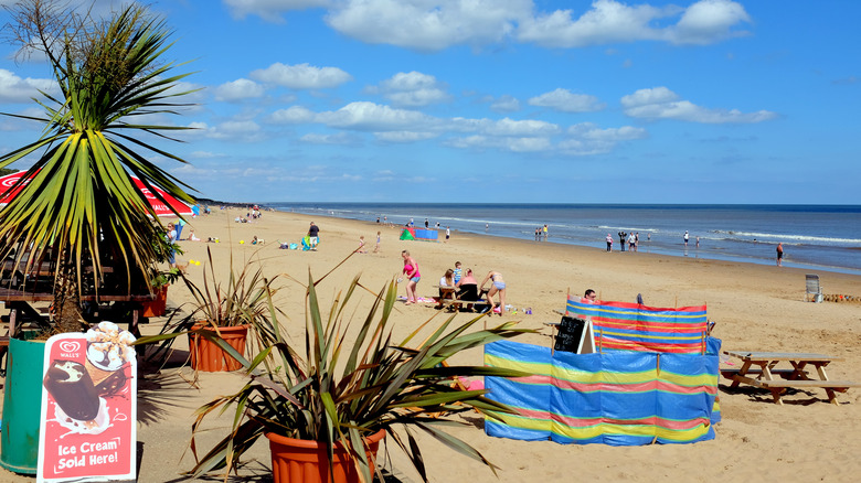 Vacationers enjoying the beach and sea in Mablethorpe, England, with ice cream stands and picnic tables on the shore