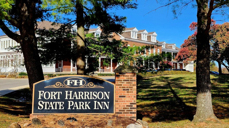 A brick sign in front of a brick and white hotel, the Fort Harrison State Park Inn in Indiana