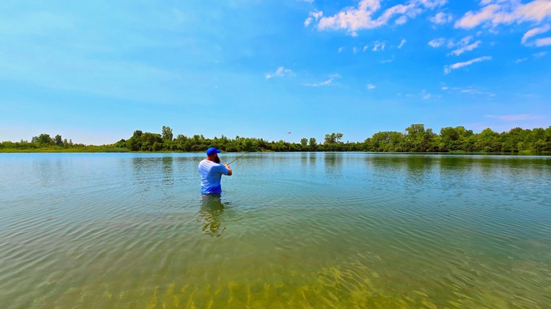 A man standing in shallow water with a fishing rod at River Bend Forest Preserve, Illinois