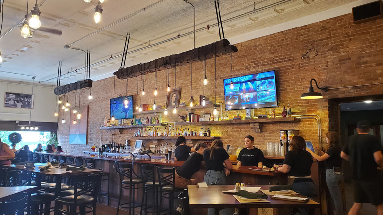 Interior of Blind Society, with brick walls, people standing around bar, and televisions