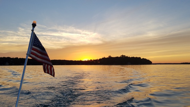 U.S. flag flying on a pole against sunset at Gull Lake, Michigan, with a boat making waves