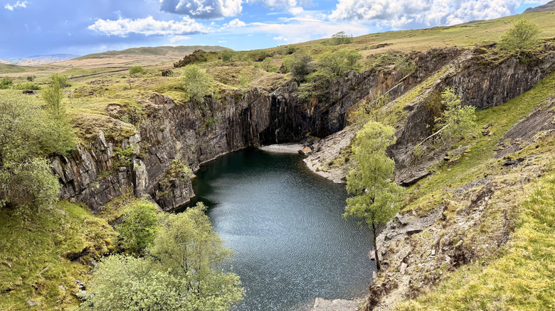 Abandoned quarry surrounded by rock cliffs and green trees on a cloudy day at Coniston, Lake District National Park, England