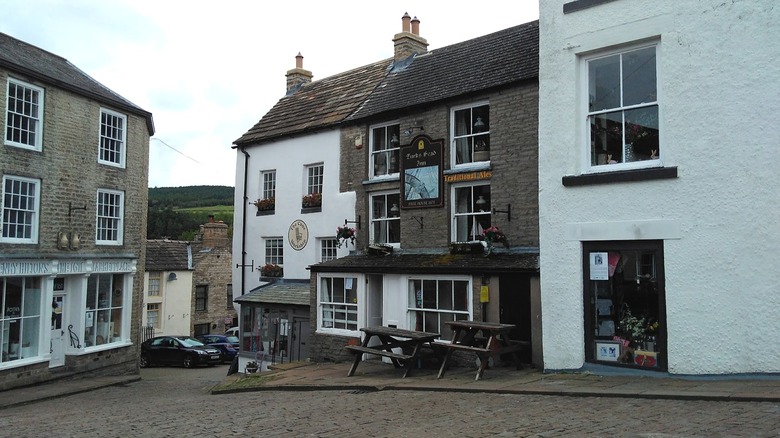 Picnic tables, a stone pub, and pretty stores on a cobblestoned street in Alston