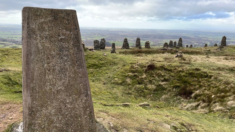 Ancient stones and cairns on a grassy hill with fields, meadows, and trees in the distance