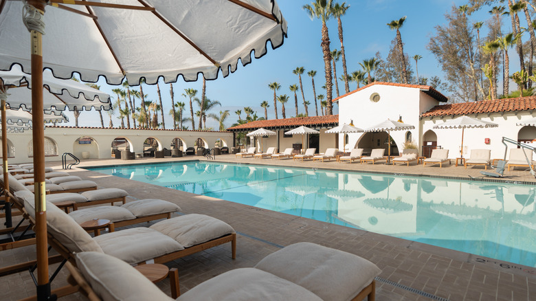 View of outdoor pool during the day with lounge chairs surrounding and trees in the background at Murrieta Hot Springs Resort