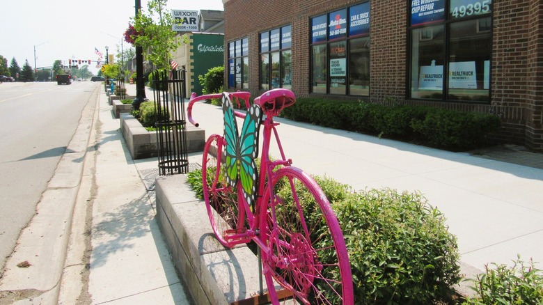 sidewalk in Wixom with businesses and pink bike art installation in foreground