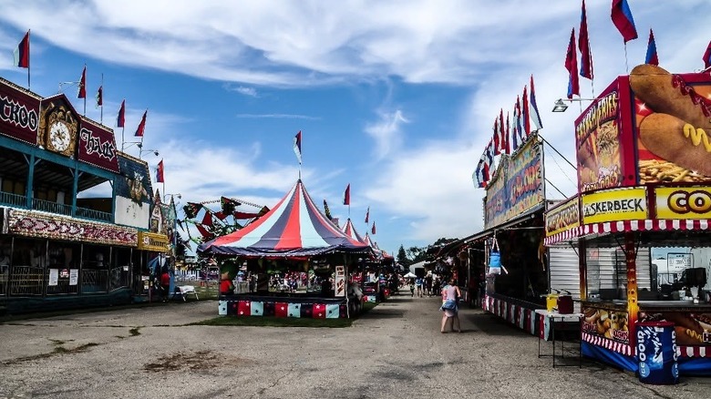 Festival with food booths and red, white, and blue striped tents under a blue sky