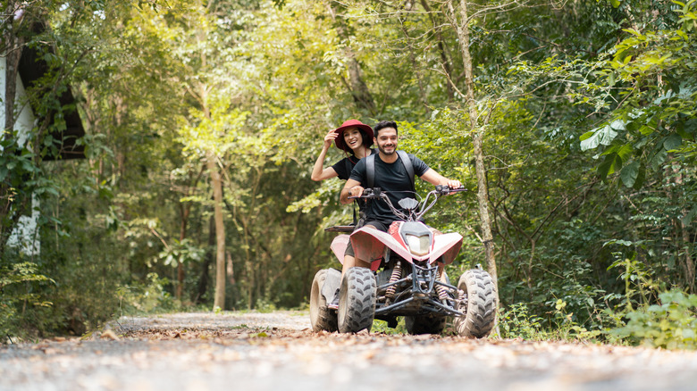 A young couple driving ATV quad bike on a trail in the woods.