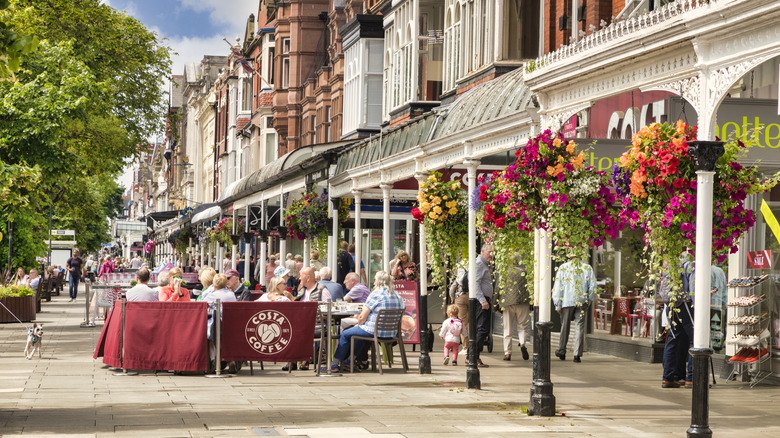 View of Lord Street in Southport, UK in spring, with baskets of flowers hanging from eaves and people sitting at an outdoor cafe