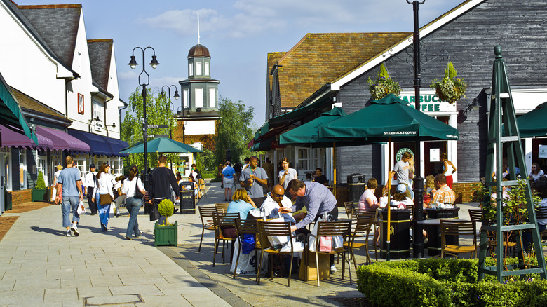 The streets Bicester Shopping village in Oxfordshire England UK on a sunny day with people sitting at cafes