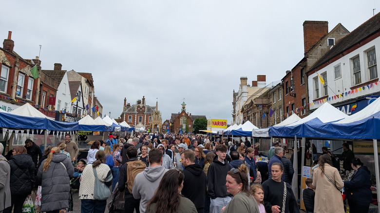The bustling Leighton Buzzard Market thronged with people, tent stalls lining both sides of the street, and historic brick buildings behind them and at the end of the street
