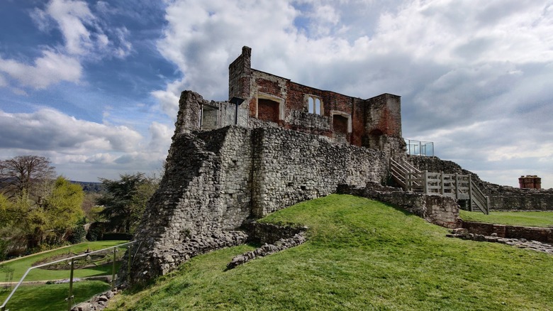 Stone castle keep ruins on a green hill under a blue and white cloud sky.