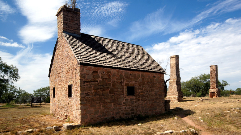 A stone building in a field with two stone chimneys in the background at Fort Phantom Hill Texas