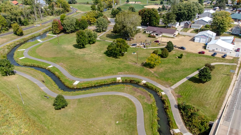 An aerial photo of Coon Valley Park with the river snaking through, walking paths on each side, and green grass of a summer day
