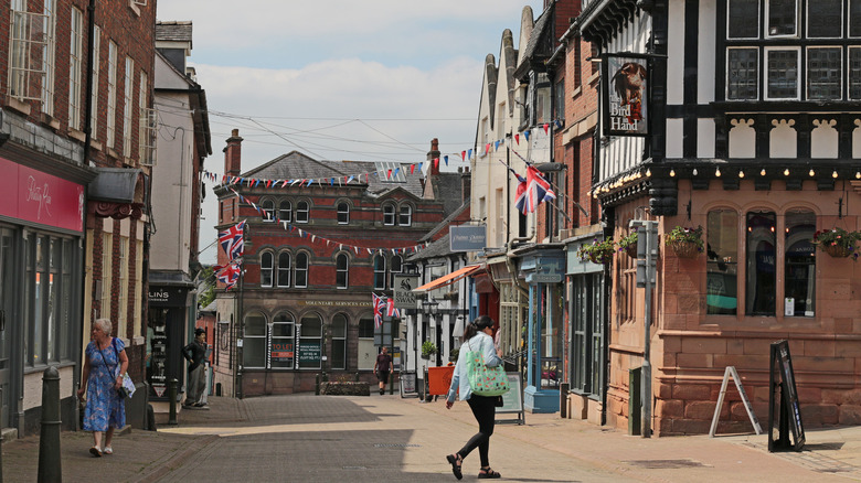 People walking down a brick road in Leek's town center with historic buildings and pubs on either side.