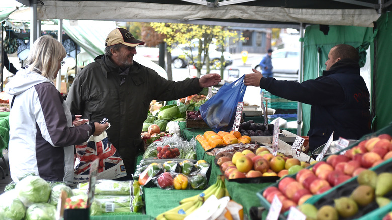 A man and woman buying fresh produce from a fruit and veg stall during a market day in Leek, England.