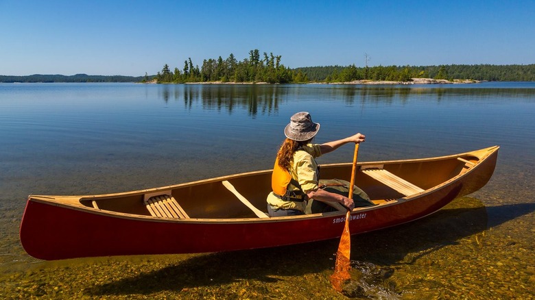 A woman wearing a hat paddling a red canoe on a calm river
