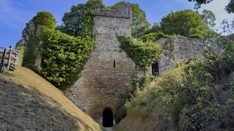 Solid stone medieval tower flanked by earth mounds with vegetation