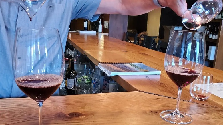 A person pouring two glasses of wine from two small glass carafes at the bar in Waterford Wine & Spirits.