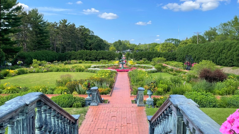 The legeant Munsinger Clemens Gardens with a brick pathway lined with flower beds and leading to a circular fountain