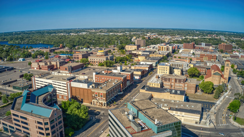 An aerial view of St. Cloud, Minnesota with downtown brick buildings, scattered green trees, and a touch of the Mississippi River to the left